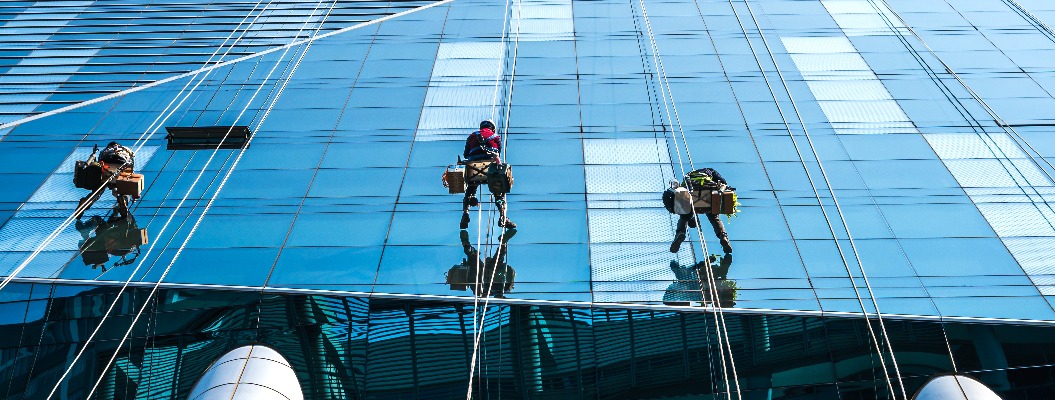 Gruppe von Hochhausarbeitern, die an einem Zugangsseil hängen und ein gläsernes Hochhaus in Seoul, Südkorea, reinigen