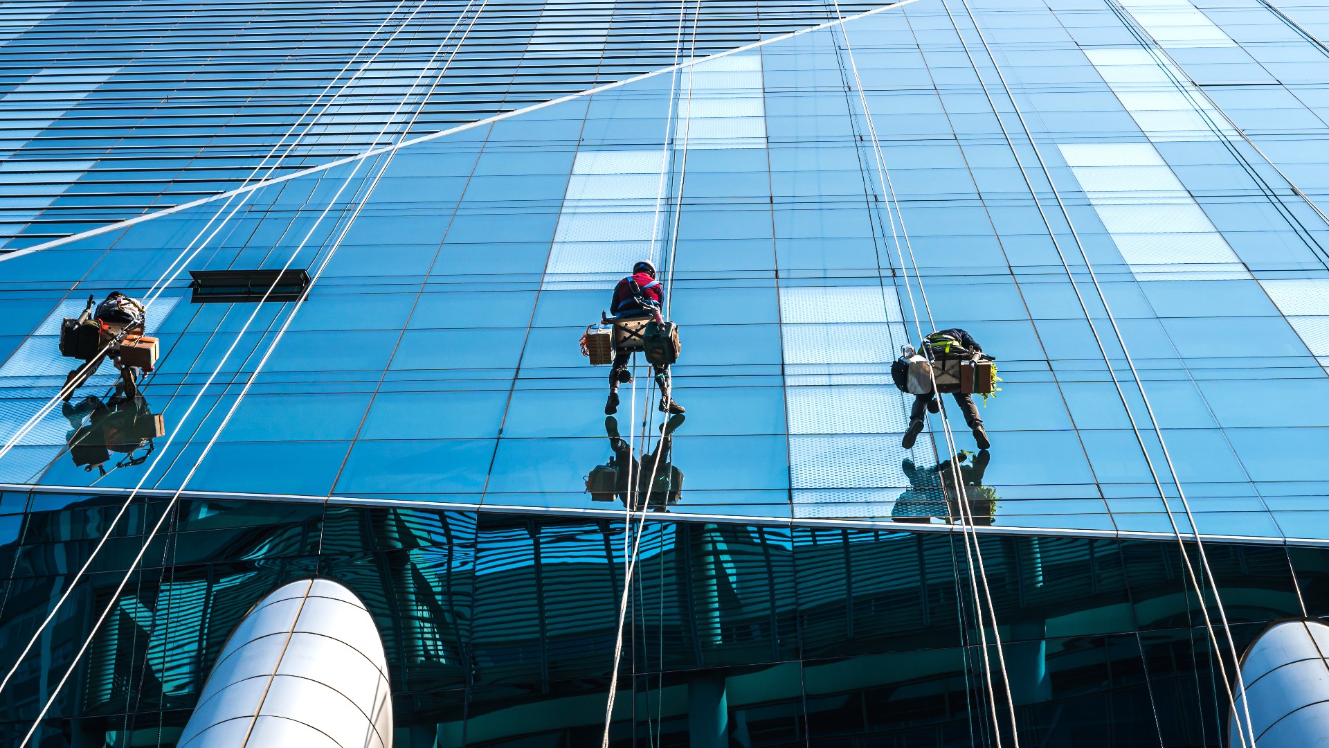 Gruppe von Hochhausarbeitern, die an einem Zugangsseil hängen und ein gläsernes Hochhaus in Seoul, Südkorea, reinigen